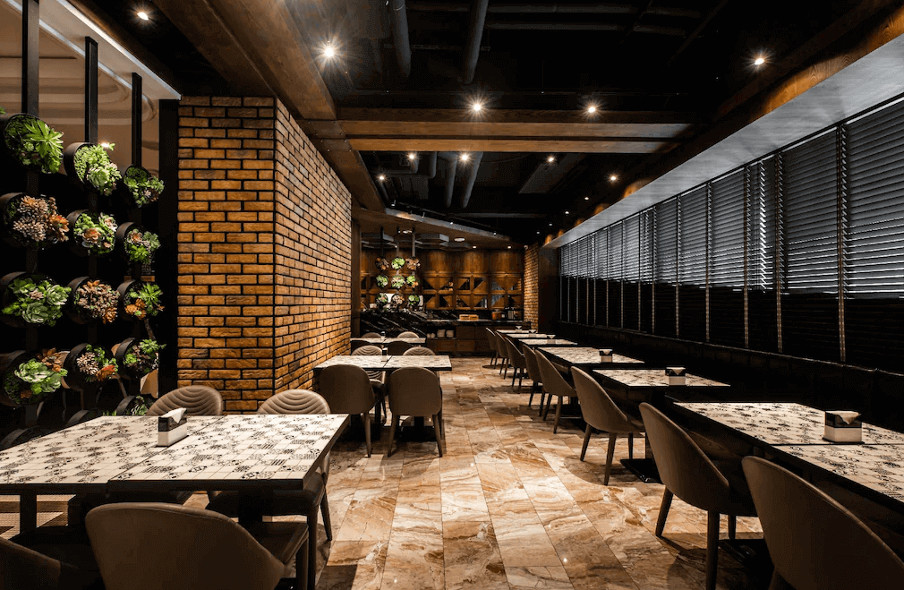 【台中火車站住宿】「挪威森林台中文創館的餐廳空間，採用磚牆、木質樑柱與暖色燈光打造工業設計風，餐桌旁設有綠植裝飾，營造舒適自然的用餐氛圍。」