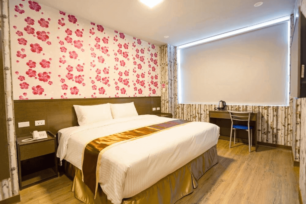 【台中火車站住宿】「撲克商旅雙人房，房內以粉紅花卉壁紙與木質地板打造溫馨風格，設有大床、書桌與簡約木質家具。」