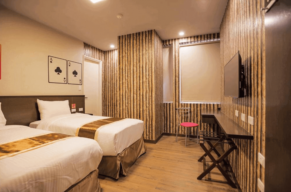【台中火車站住宿】「撲克商旅雙床房，房內以撲克主題裝飾與木紋牆面設計，配備兩張單人床、書桌與壁掛電視。」