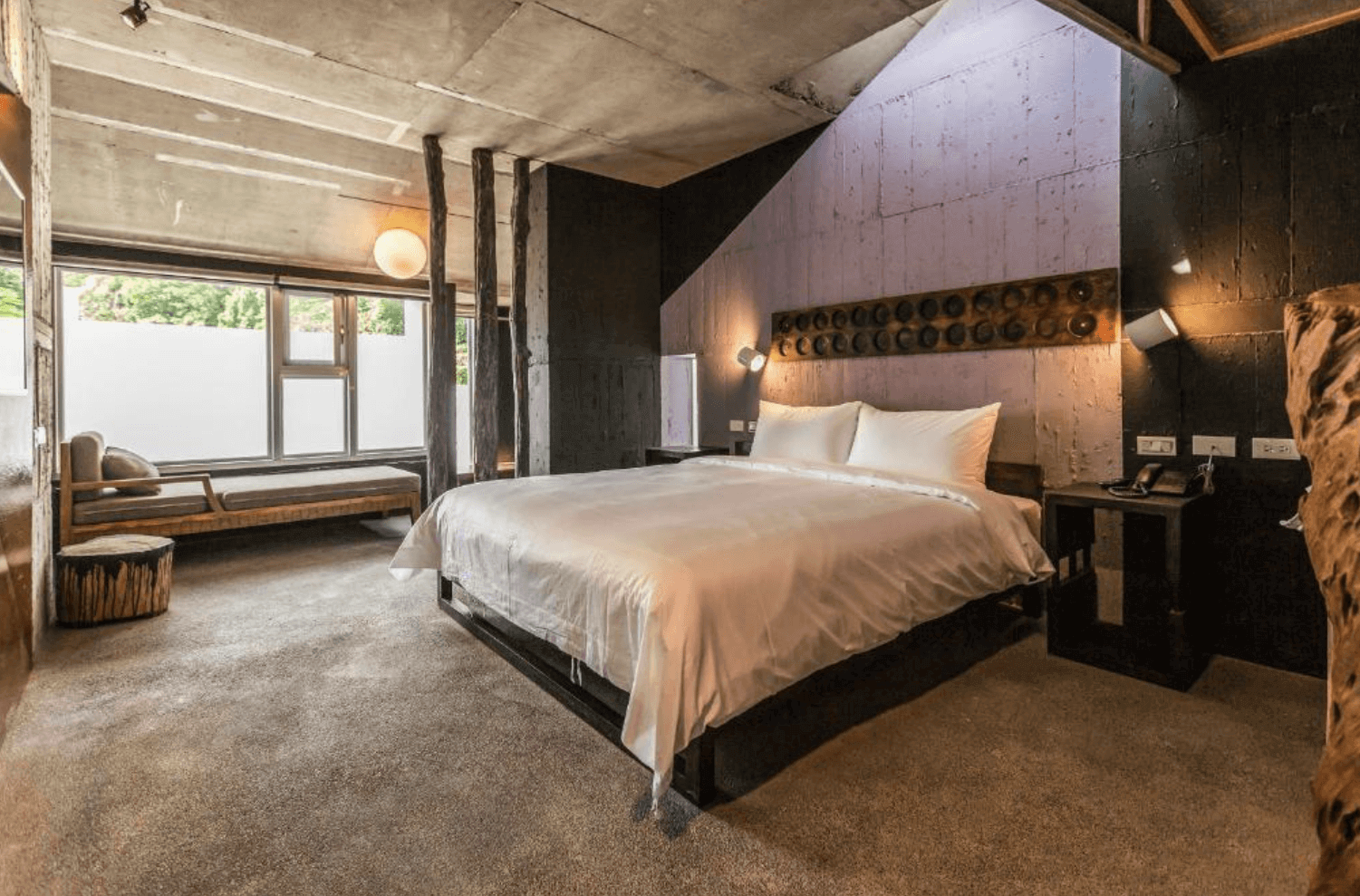 【宜蘭溫泉飯店】「有朋會館雙人房，房內以大量原木元素、手作感裝飾與清水模牆面營造大地質感，搭配大床與落地窗邊休憩座位，呈現沉穩自然的住宿空間。」