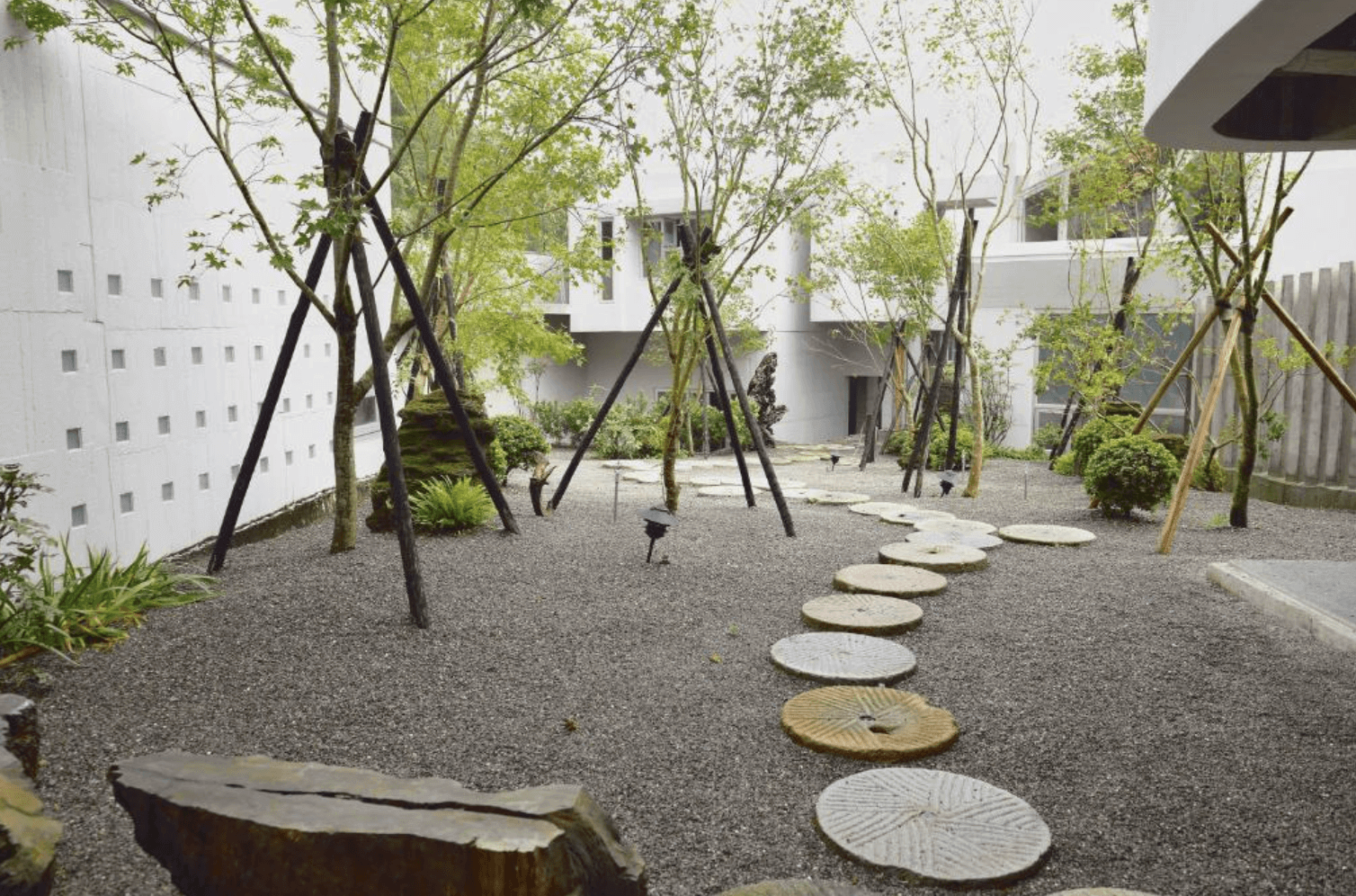 【宜蘭溫泉飯店】「有朋會館戶外庭園，以白砂與石板步道搭配多株植栽打造禪風意境，可見散落的青苔岩石與自然光影，呈現靜謐的日式庭園氛圍。」