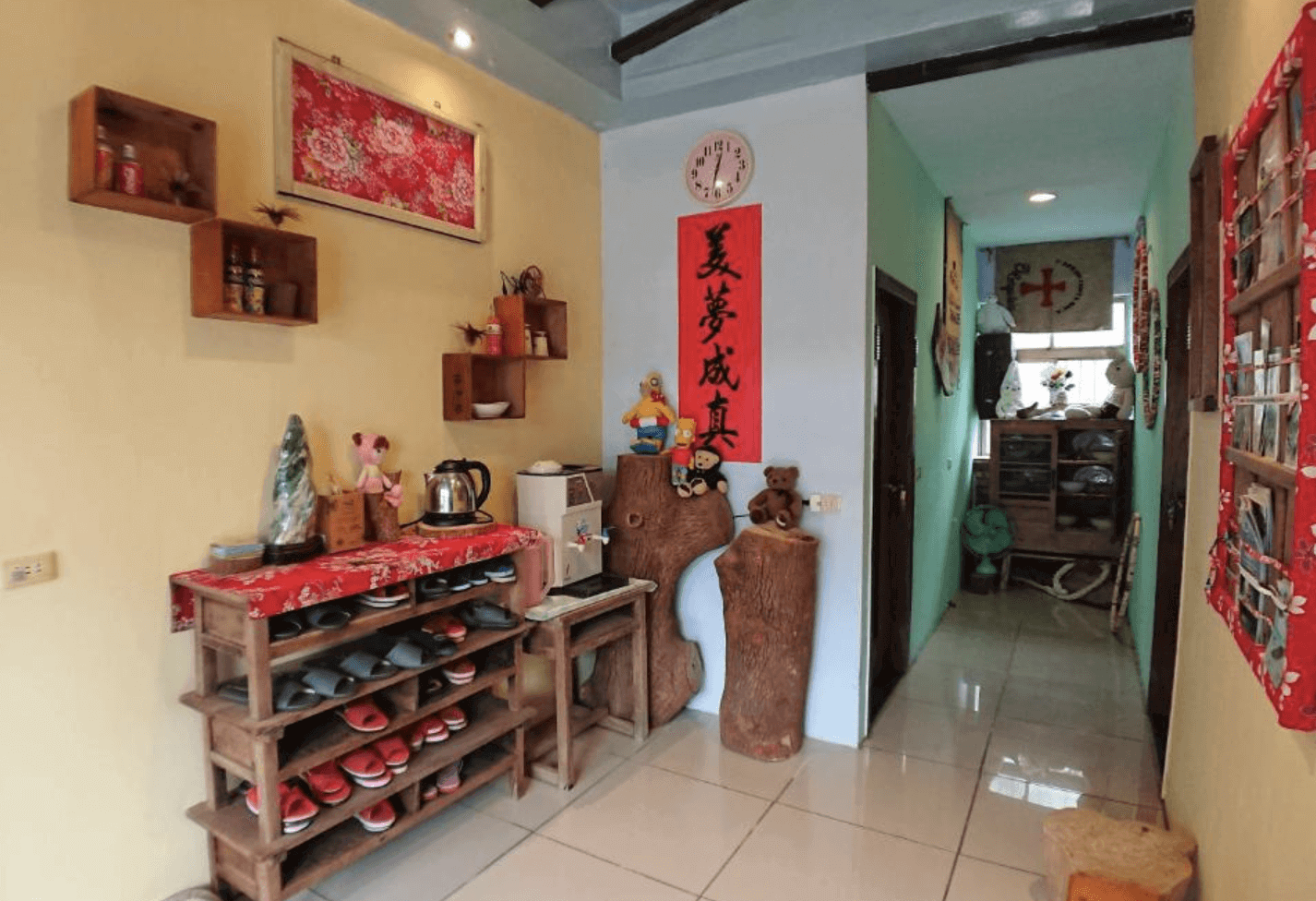【東華大學民宿】「東華八號民宿」公共空間，入口擺放木質鞋架與熱水壺設備，牆上懸掛紅色書法春聯與花布裝飾，充滿濃厚台灣懷舊風情與人情味。