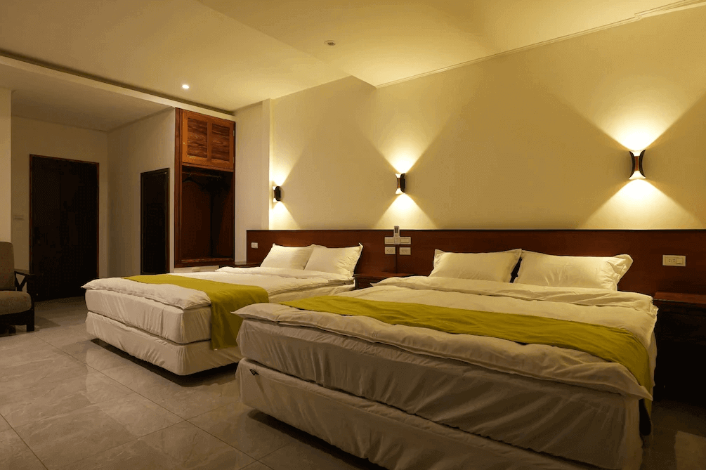 【大溪住宿】樂木居 河岸行館 四人房，兩張大床設計寬敞舒適，牆面暖黃光線營造放鬆氛圍，房內備有衣櫃與休憩椅。