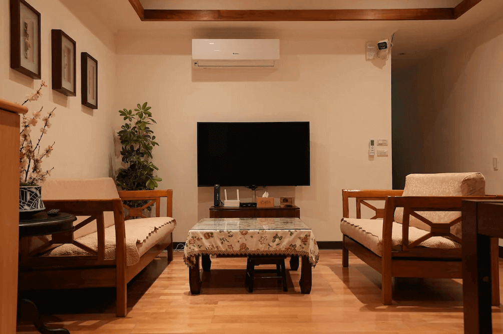 【大溪住宿】樂木居 河岸行館 公共客廳，木質家具與米色沙發搭配花布桌巾，溫馨典雅的空間設有大螢幕電視與舒適座位區。