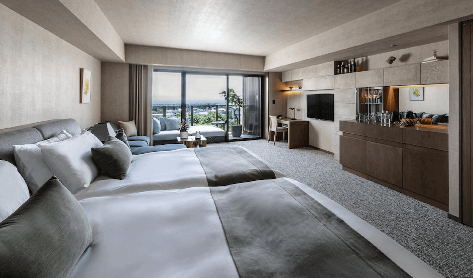 【讀谷村住宿】「沖繩讀谷 GLAMDAY STYLE 酒店及度假村的高級雙床房，房內以柔和米色與木質調打造沈穩質感，設有沙發休憩區與大片落地窗，可眺望戶外景致。」