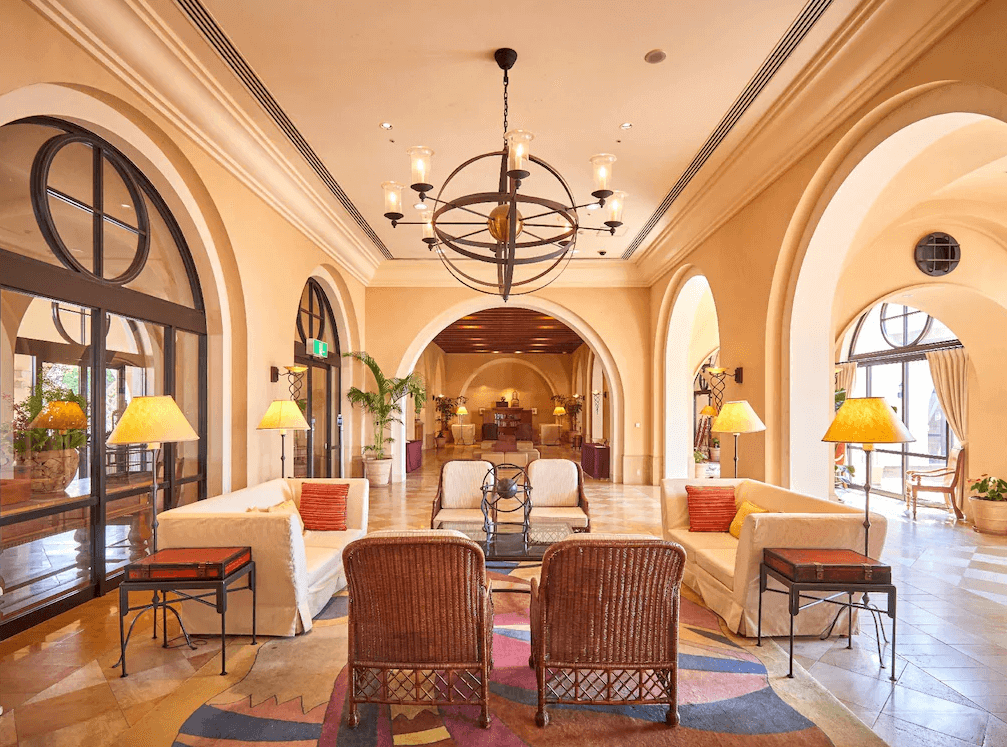 【讀谷村住宿】「沖繩阿利比拉日航度假飯店的大廳，以西班牙風格拱門、溫暖燈光與藤編家具打造優雅度假氛圍，是旅客放鬆休憩的迎賓空間。」