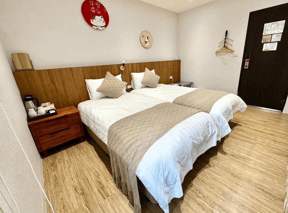 【大溪住宿】湧山水民宿 雙人房，兩張單人床鋪整潔明亮，木質地板搭配溫暖燈光，牆上掛有招財貓與日式裝飾畫，氛圍溫馨可愛。