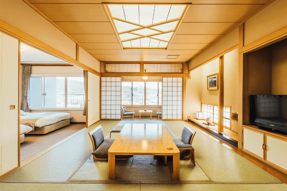 【北見住宿】"北見住宿精選示意圖"溫根湯溫泉美肌之湯宿大江本家的傳統和式房，榻榻米地板與木質拉門設計，搭配矮桌與坐墊，窗外可見山景，充滿濃厚日式風情。