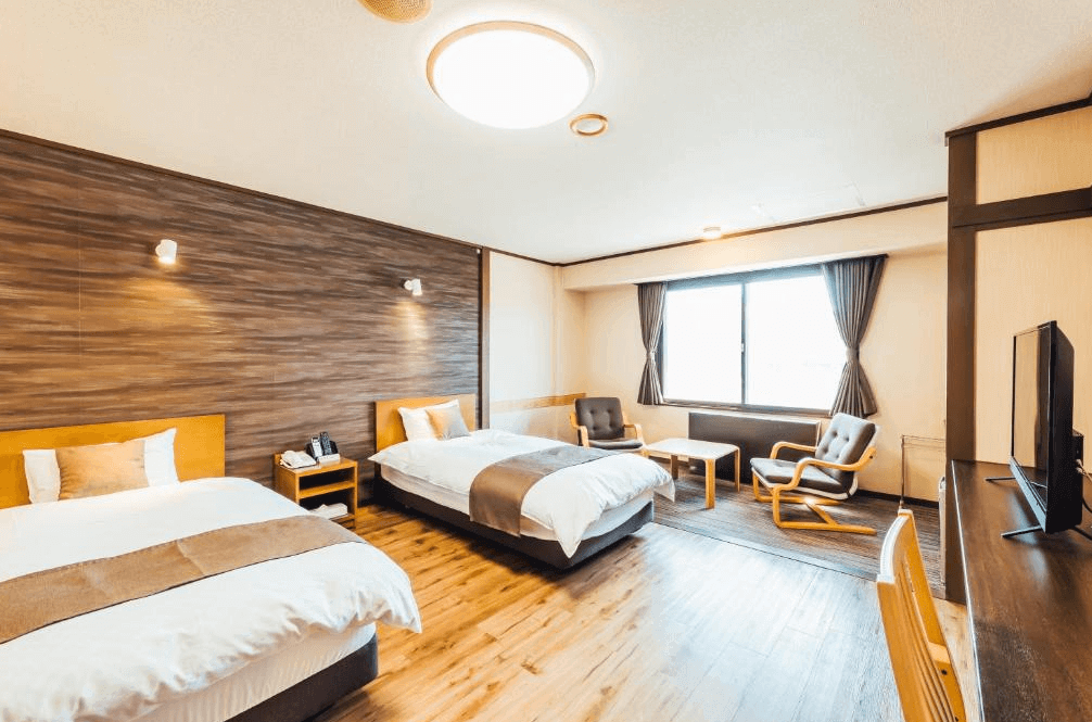 【北見住宿】溫根湯溫泉美肌之湯宿大江本家的洋式雙床房，房間以木質色調為主，搭配大面窗戶與休憩沙發區，空間明亮舒適。