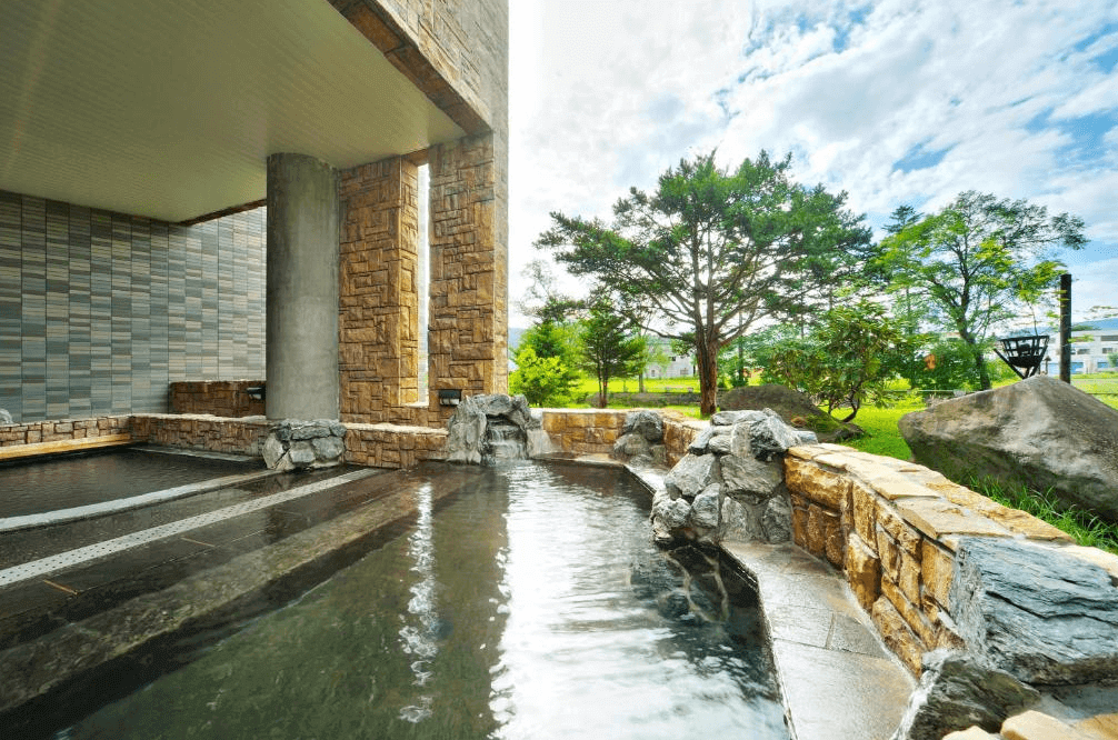 【北見住宿】溫根湯溫泉美肌之湯宿大江本家的露天溫泉池，石造圍欄搭配自然景觀，能在青空與綠樹環繞下泡湯放鬆，感受大自然療癒氣息。