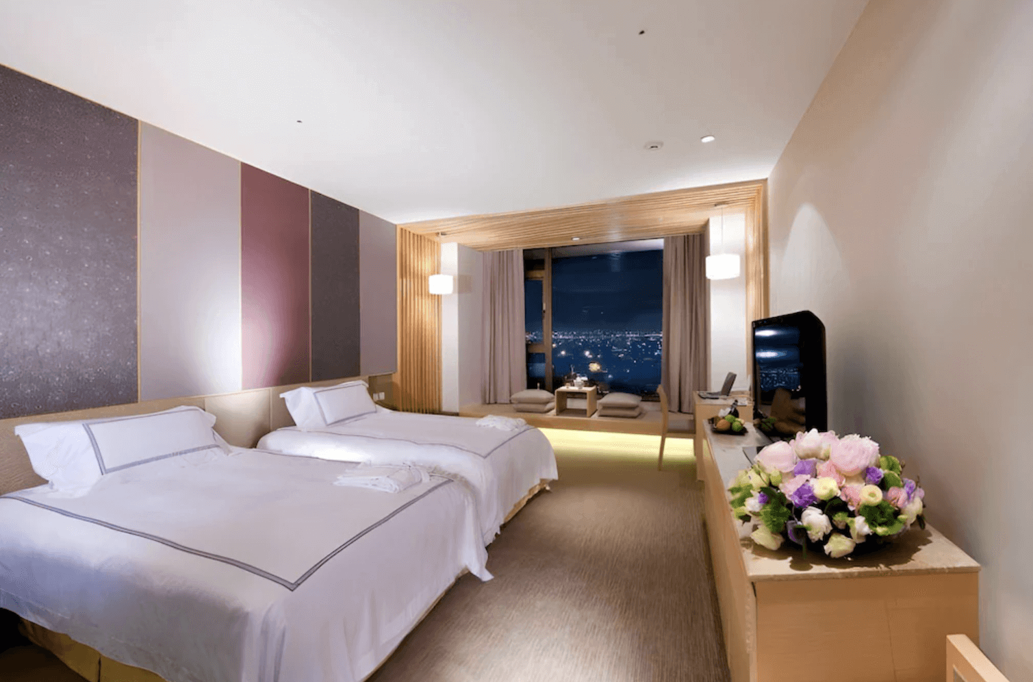 【宜蘭溫泉飯店】「礁溪長榮鳳凰酒店雙床房內景，客房以柔和木質調與暖色燈光呈現，前方設有大片落地窗與和式休憩區，可俯瞰夜景，整體空間寬敞舒適。」