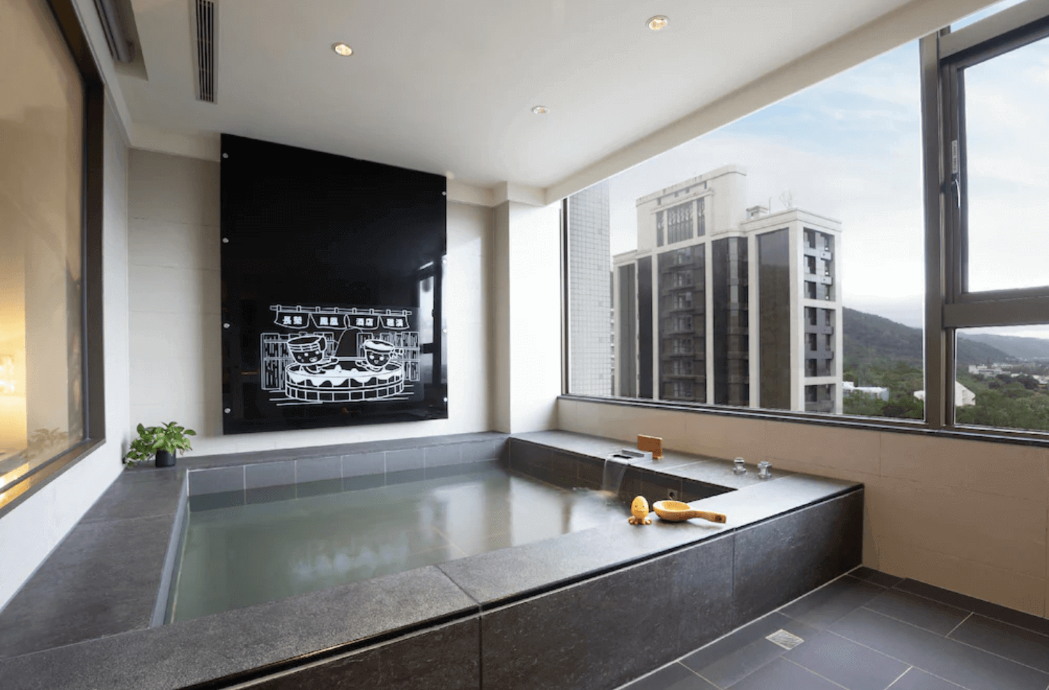 【宜蘭溫泉飯店】「礁溪長榮鳳凰酒店客房內的私人溫泉浴池，採大面窗景設計，可眺望山景與建築群，浴池以深色石材打造，空間明亮放鬆。」