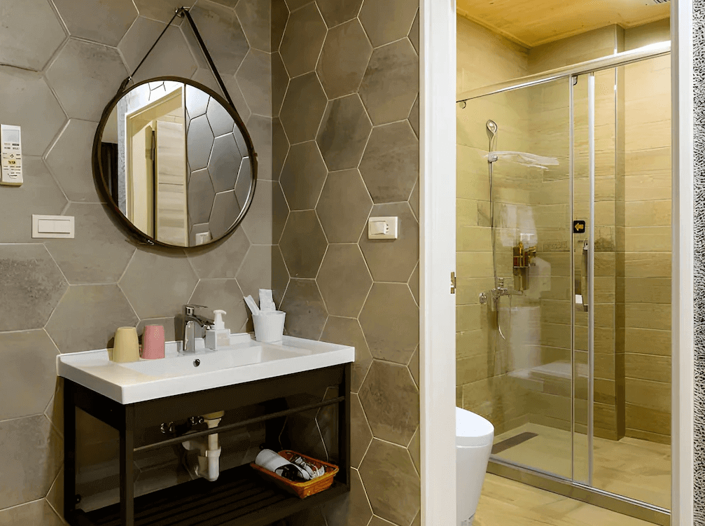 【大溪住宿】秘境41民宿 浴室空間，六角磚牆面搭配木紋地板，設有圓形鏡面與乾濕分離玻璃淋浴間，整潔現代且具設計感。