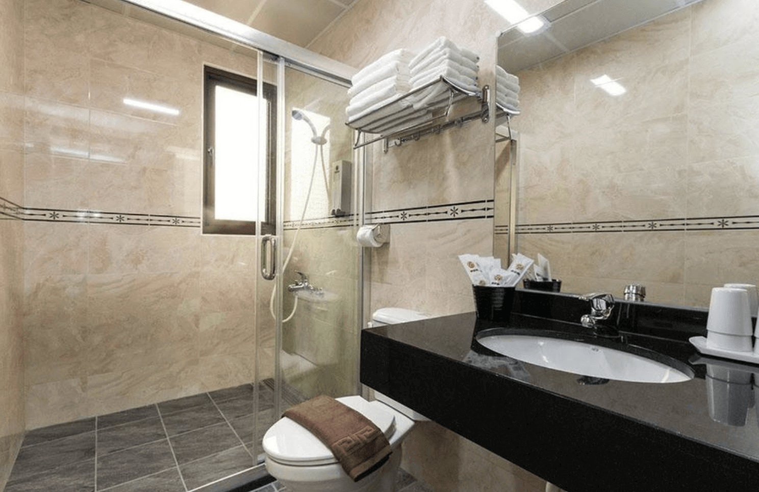 【東華大學民宿】「童樂會親子民宿」浴室空間，採用米色大理石紋磁磚與黑色檯面設計，乾濕分離、備有盥洗用品與毛巾，整體明亮乾淨。