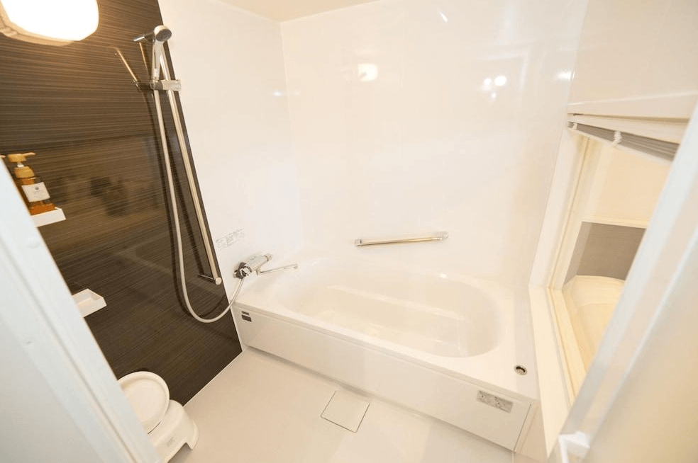 【奄美大島住宿】「美阿丹海灘飯店浴室：白色明亮的浴室空間，配有浴缸、花灑淋浴與貼心扶手，整體乾淨整潔。」