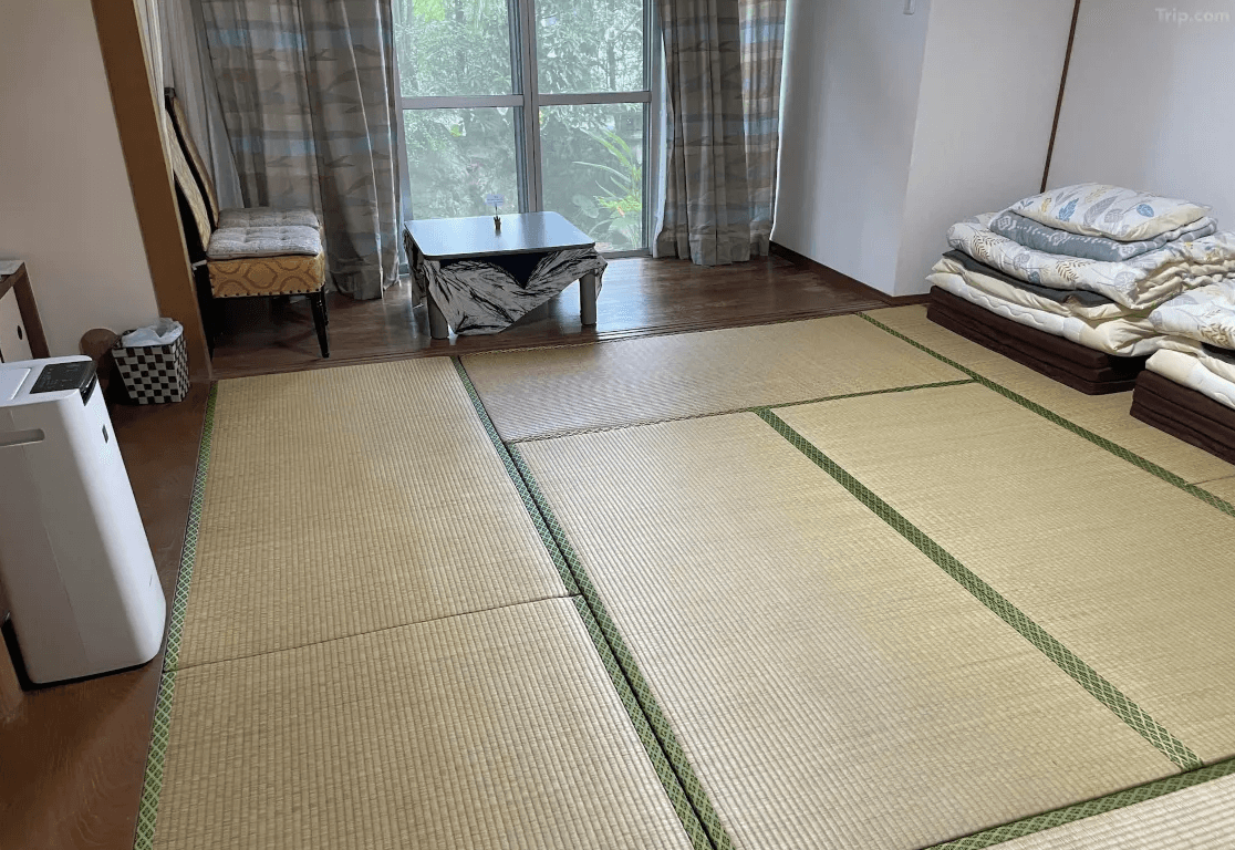 【奄美大島住宿】「花海house（Kami House）和室房：大片榻榻米空間，附有疊放整齊的日式床墊與和室桌椅，可欣賞窗外綠意景致。」