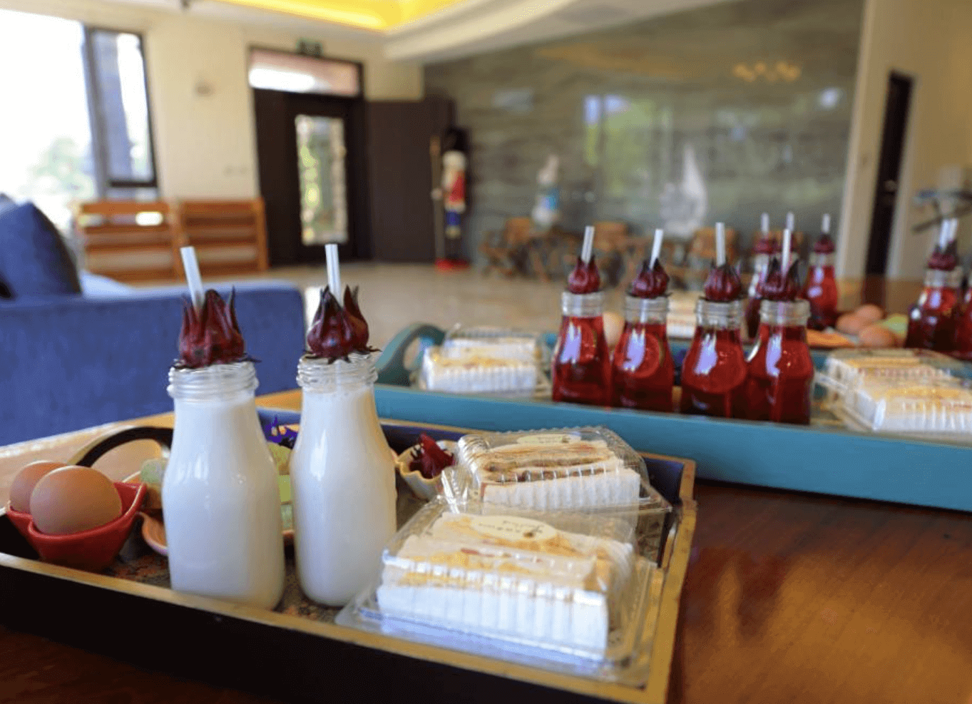 【東華大學民宿】「花綠蒂庭園民宿」迎賓茶點，提供洛神花飲、鮮奶、蛋與精緻蛋糕，擺放於民宿大廳木桌上，展現貼心與溫馨的款待氛圍。