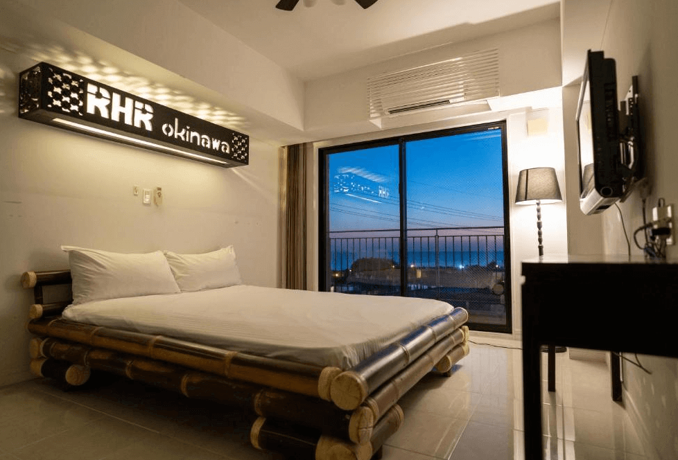 【讀谷村住宿】「讀谷皇家飯店的海景房，房內以竹架造型床架打造自然風格，落地窗外可欣賞夜色與海景，呈現寧靜愜意的住宿氛圍。」