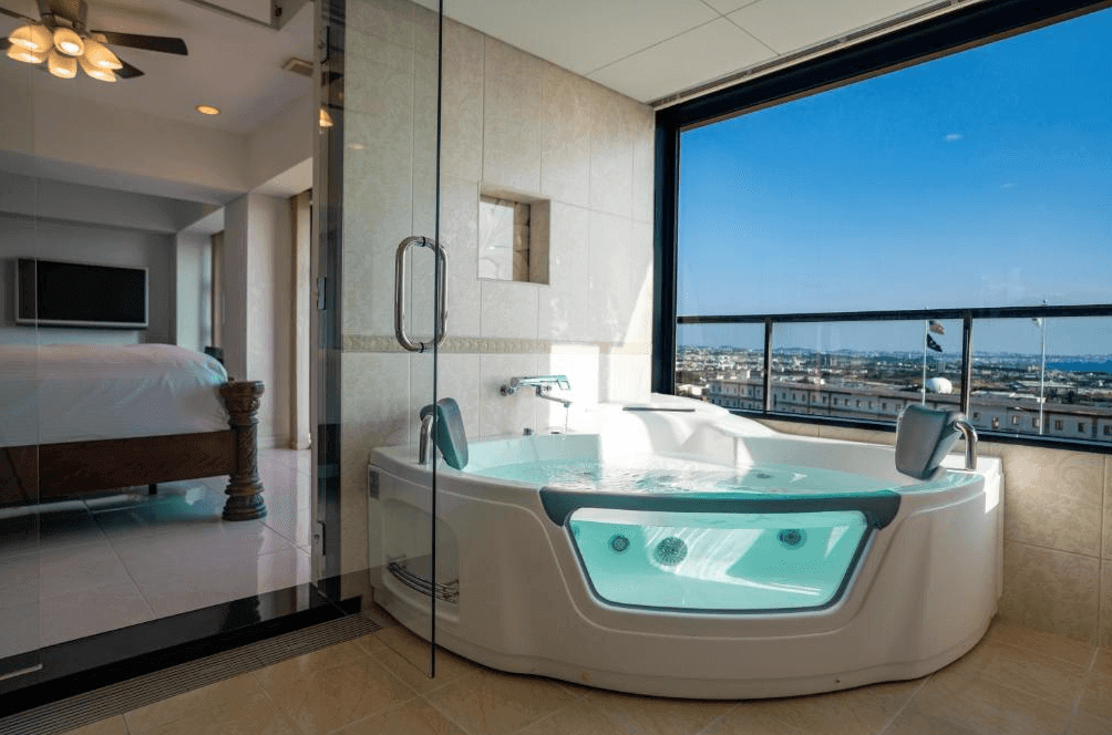 【讀谷村住宿】「讀谷皇家飯店的景觀按摩浴缸房型，浴缸旁設有大面玻璃窗，可一邊泡澡一邊欣賞城市與海岸線全景，空間明亮舒適。」