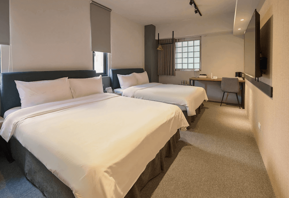 【台中火車站住宿】「逗點 inn Hotel 的家庭房，提供兩張大床與寬敞空間，採用暖色燈光與極簡設計，並設有書桌與衣架吊掛區，適合家庭或朋友入住。」