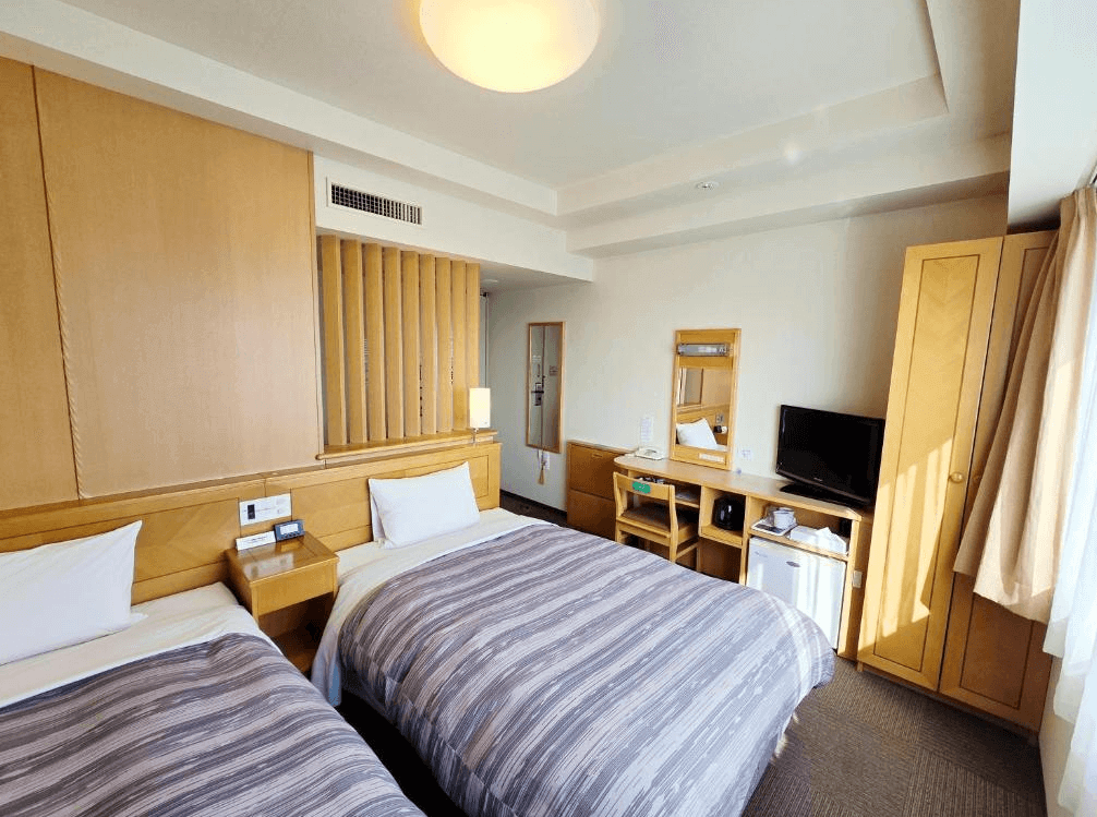 【北見住宿】露櫻酒店北見大通西店的雙床房，採用明亮木質設計，房內設有電視、書桌、小冰箱與大片窗戶，整體空間乾淨舒適、光線充足。