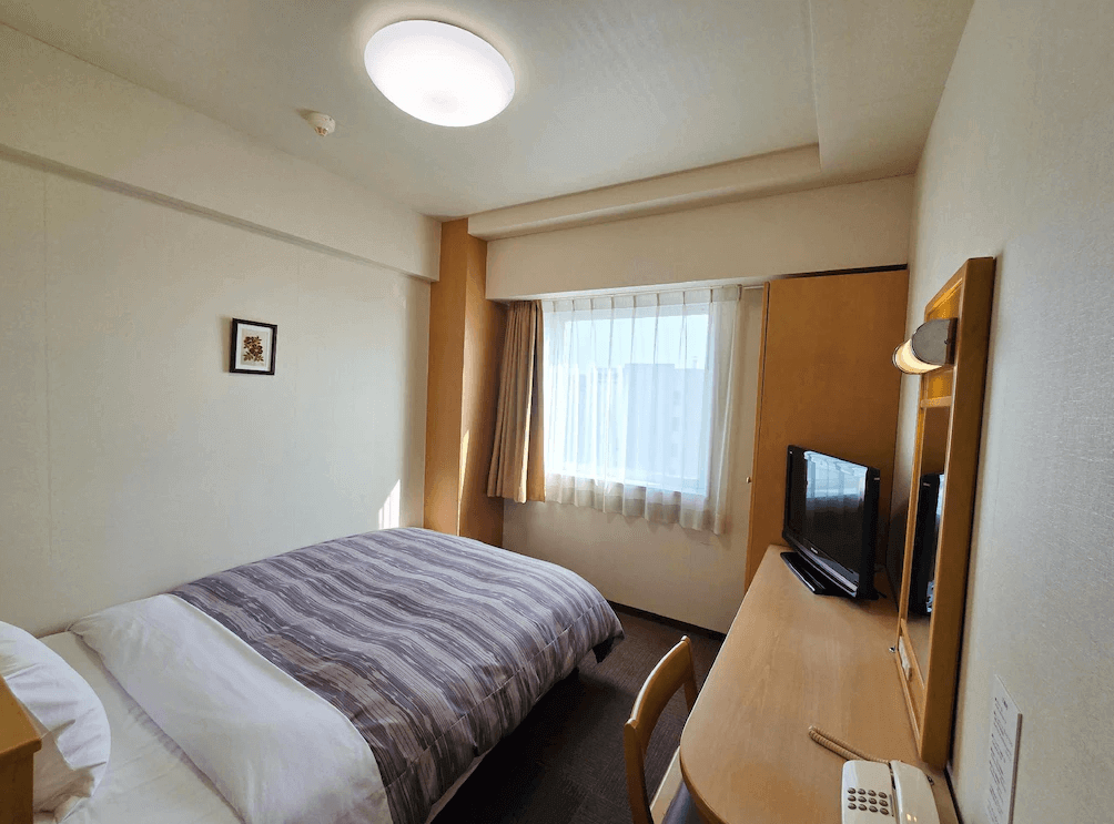 【北見住宿】露櫻酒店北見大通西店的單人房，配置一張雙人床與書桌區，窗邊採光良好，房間設計簡約溫馨，適合商務與獨行旅客。