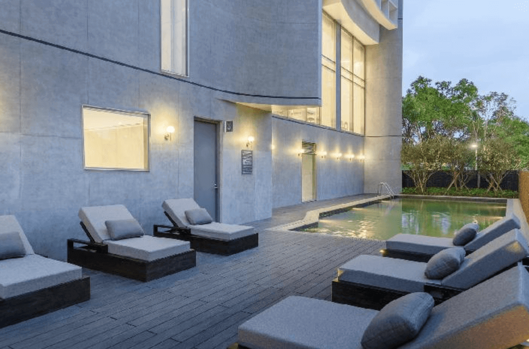 【宜蘭溫泉飯店】「風華渡假酒店・礁溪館戶外溫水泳池與躺椅區，周圍灰色建築牆面搭配暖色壁燈，營造安靜放鬆的泳池空間並附有多張舒適躺椅。」