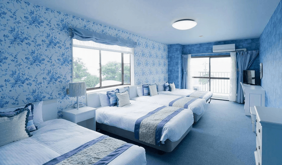 【奄美大島住宿】「龍美 Caretta 飯店（Hotel Caretta Amami）的家庭房，房內以藍白花紋為主題，配有多張雙人床與大面採光窗，呈現清新海洋風格。」