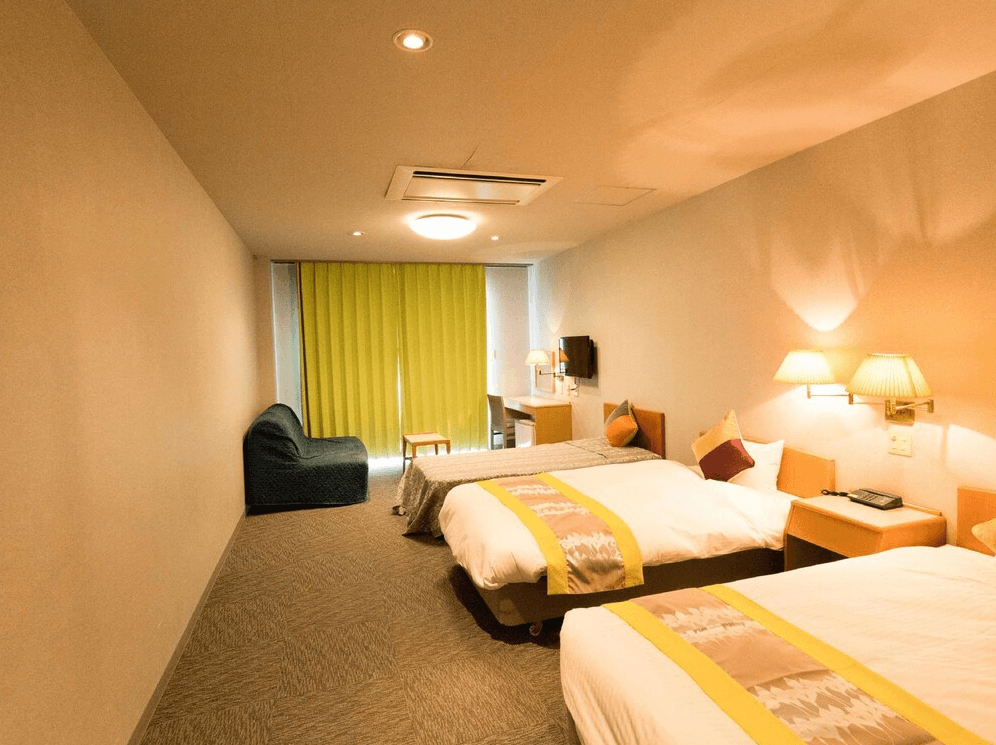 【奄美大島住宿】「龍美 Caretta 飯店（Hotel Caretta Amami）的雙床客房，房內設計以黃色與淡色系為主調，含沙發與工作桌，空間寬敞舒適。」