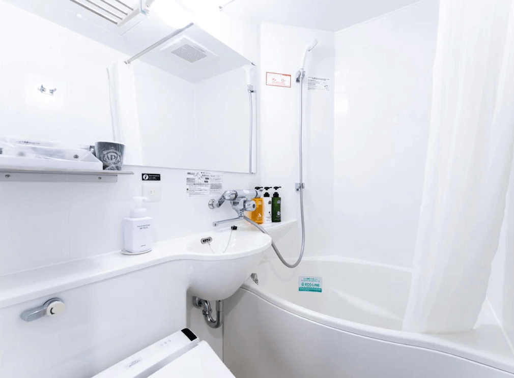【霧島住宿】APA 飯店的客房浴室：APA 飯店客房內的標準模組化浴室，包含一個浴缸、淋浴設備、洗手台、鏡子和免治馬桶。