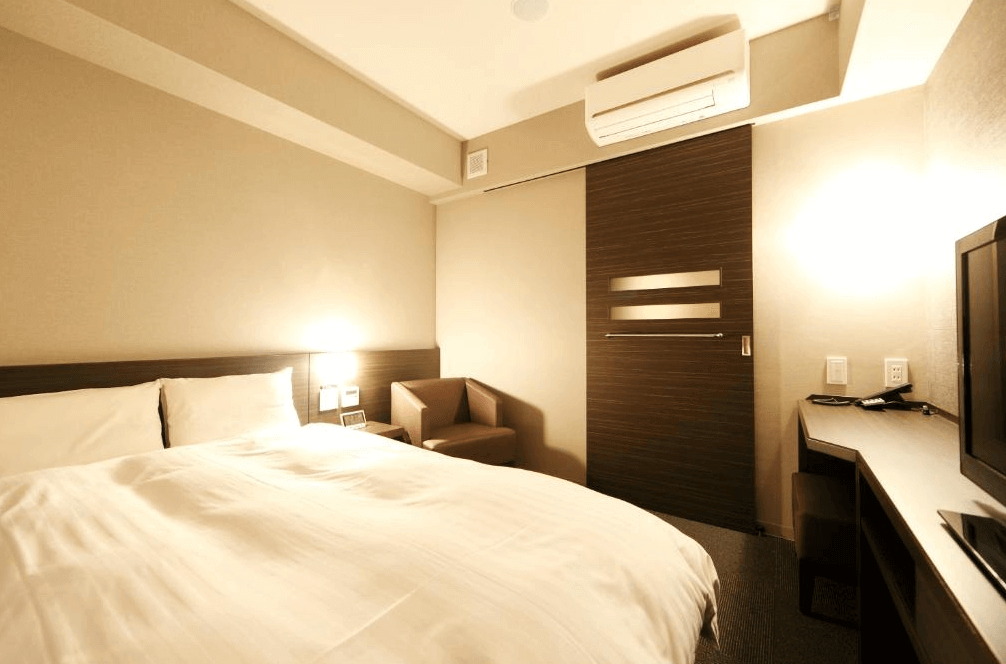 【鹿兒島住宿】Dormy Inn飯店-鹿兒島天然溫泉 的標準雙人房，配備一張舒適大床，房內風格簡約，設有深色木紋拉門與實用的長條形書桌區，空間機能完善且溫馨。