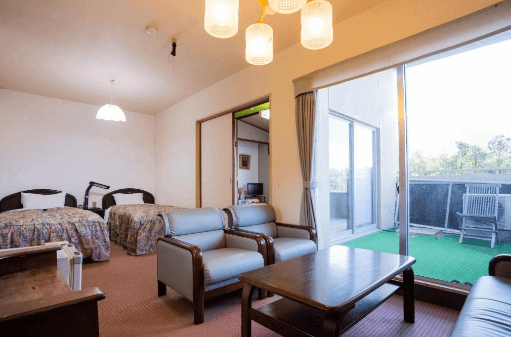 【屋久島住宿】「Hotel Yakushima Sanso 西式雙床客房，設有獨立客廳座位區與大片落地窗，可通往戶外陽台，房間空間寬敞明亮。」