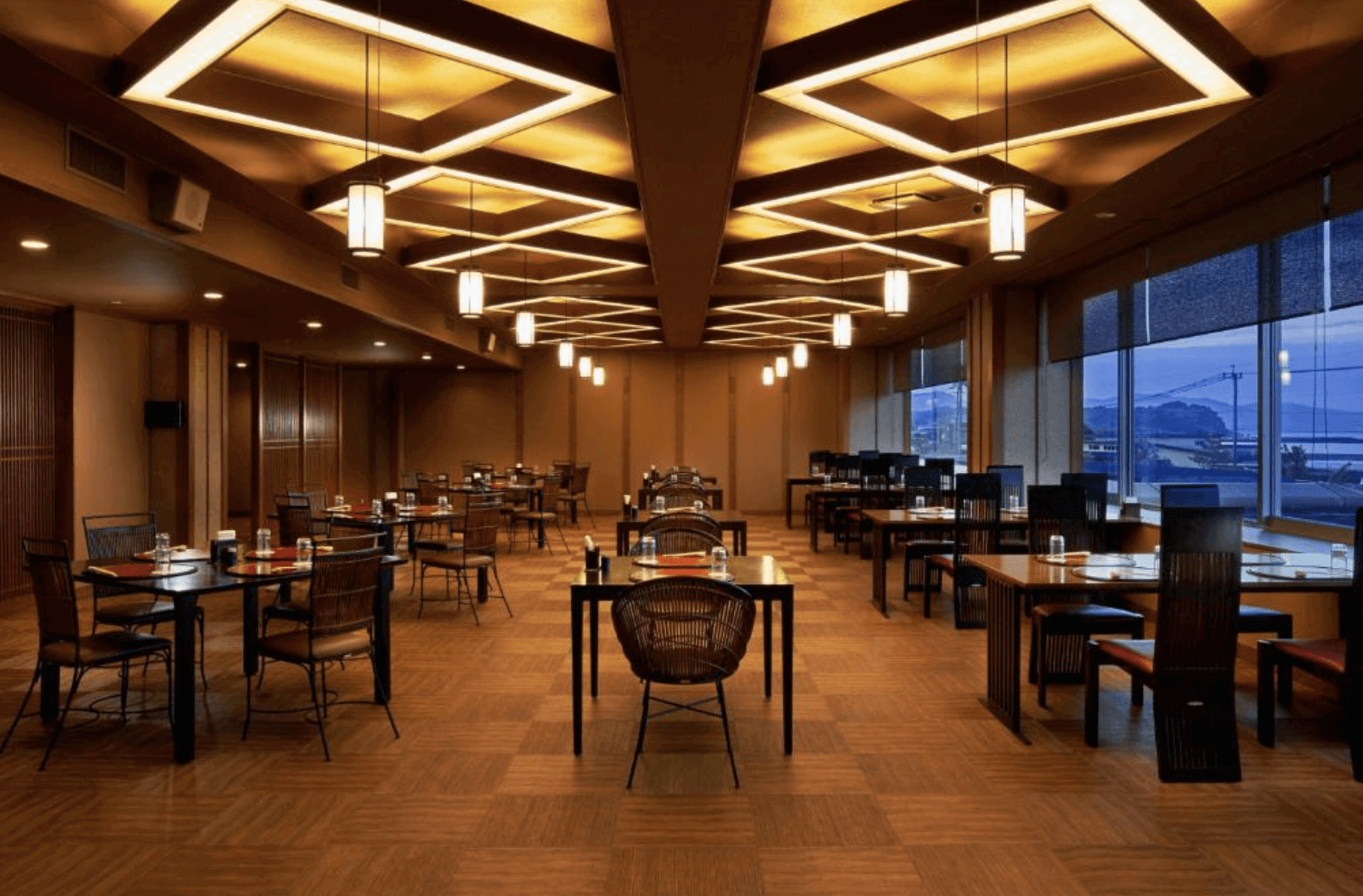 【指宿住宿】Koran之湯錦江樓 (Ryokan Koran no Yu Kinkouroh) 的用餐空間，天花板採用獨特的幾何方格照明設計，搭配深色木質桌椅，營造出溫暖且高雅的日式餐飲氛圍。