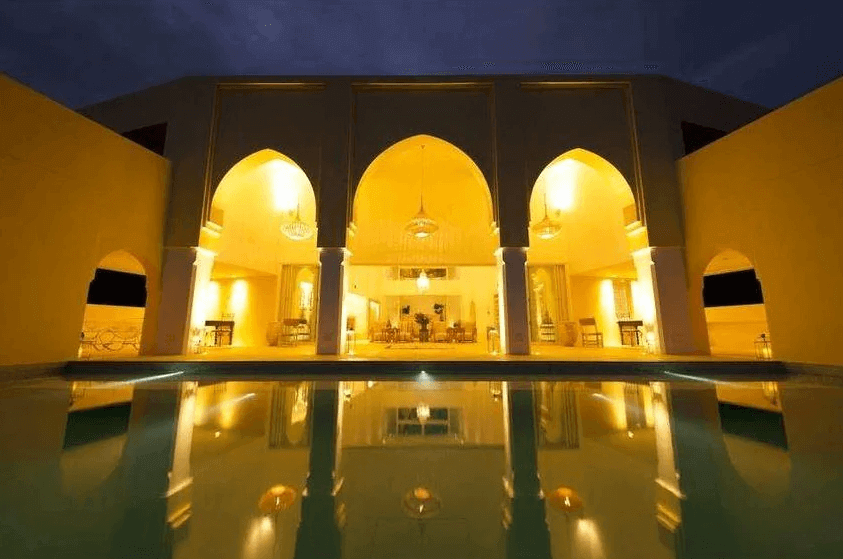 【沖繩南城住宿】Riad Lamp 的夜間庭園景致，在溫暖燈光照耀下，典型的摩洛哥拱門建築倒映在平靜的水池面上，營造出宛如一千零一夜般的夢幻宮殿氛圍。