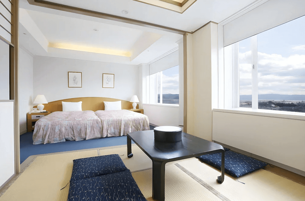 【霧島住宿】京瓷飯店的和洋式客房，結合了架高的西式雙床區與寬敞的榻榻米休憩空間，大面窗戶讓室內採光充足且視野開闊。