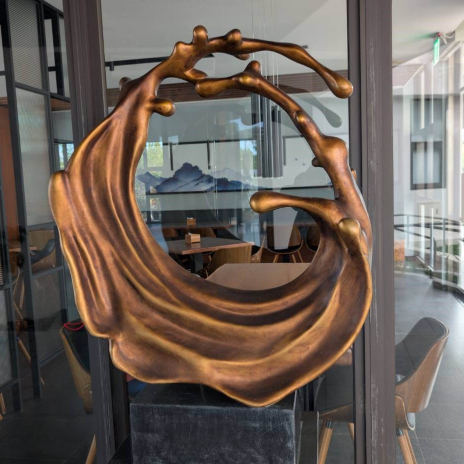 「元湯溫泉居大廳內的大型金色藝術裝置，呈現流動線條的圓弧形雕塑，背景可見落地玻璃與室內餐廳座位區。」