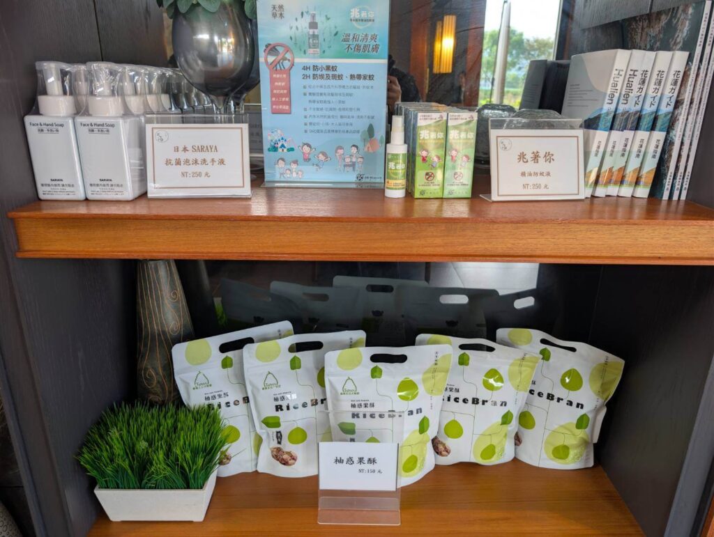 「元湯溫泉居商品陳列架，擺放日本 SARAYA 抗菌洗手慕斯、花蓮限定防蚊液、花蓮觀光指南書籍與多款米糠零食，呈現整齊清爽的販售空間。」