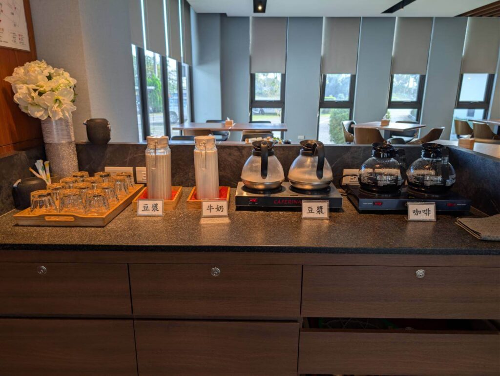 〈元湯溫泉居〉餐廳自助飲品區，提供豆漿、牛奶、熱豆漿與咖啡，桌上整齊擺放玻璃杯與飲品保溫壺。