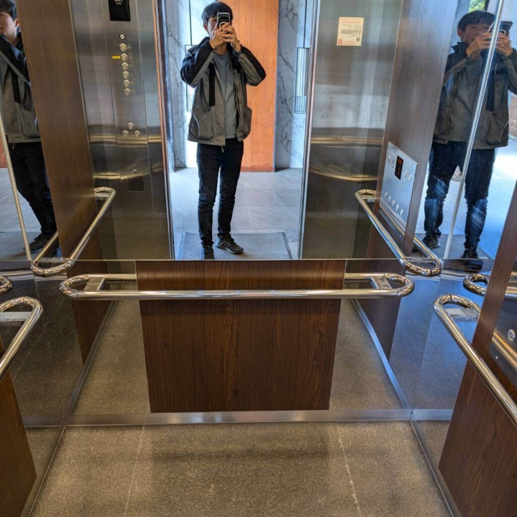 「元湯溫泉居電梯內部空間，採用木紋面板與鏡面設計，搭配不鏽鋼扶手，呈現現代簡潔的住宿設施。」