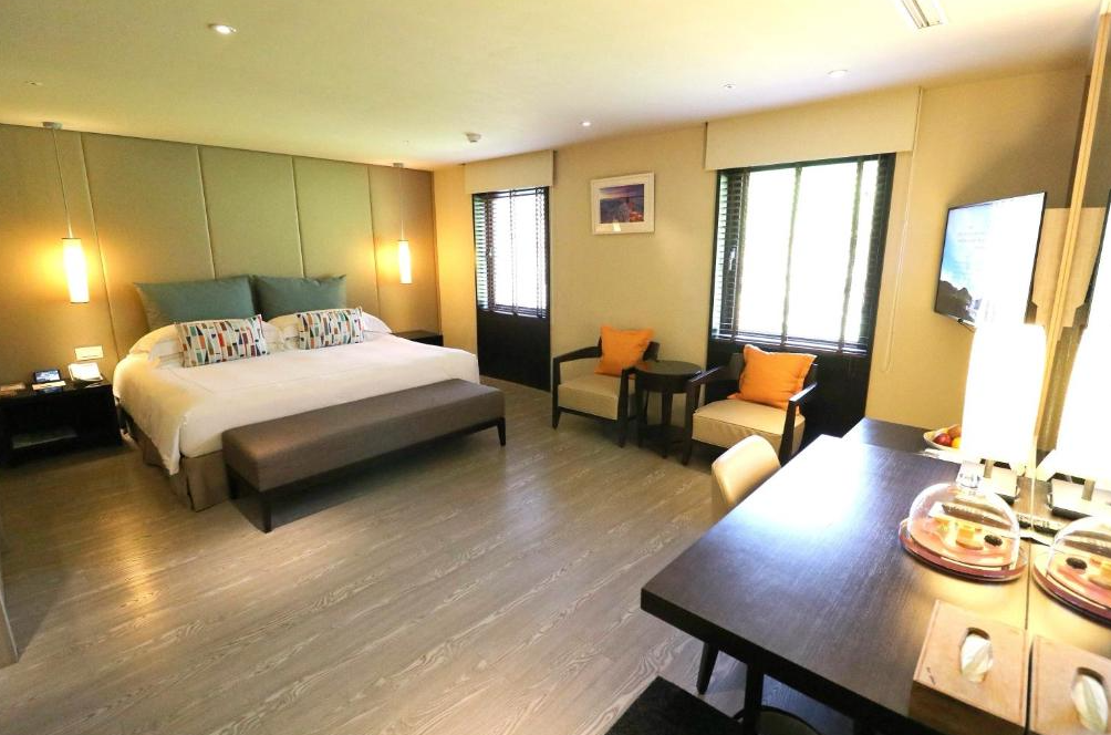 北投大地酒店 (The Gaia Hotel) 的雅緻雙床客房，設計採用溫暖的大地色系搭配活潑的橙色抱枕點綴，大面窗戶引入自然光線，營造出沉穩且放鬆的休憩氛圍。