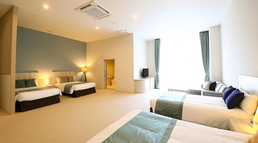【沖繩南城住宿】南城Yuinchi飯店 (The Yuinchi Hotel Nanjo) 的寬敞家庭客房，採光極佳，利用半隔間設計區分出多張舒適床鋪與起居空間，清爽的淺藍色牆面營造出放鬆的度假氛圍。