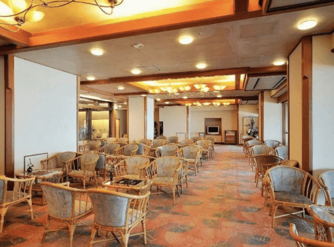 【指宿住宿】吟松花之溫泉飯店 (Hana no Onsen Hotel Ginsyo) 的大廳休息區，擺設了許多休閒藤椅，搭配暖色系的照明設計與寬敞的動線，提供旅客在泡湯後放鬆聊天或休憩的舒適場所。