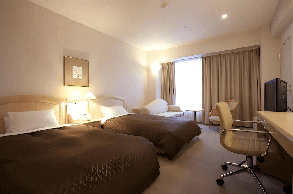 【大分住宿】大分倫勃朗酒店 (Rembrandt Hotel Oita) 的寬敞雙床客房,色調以沉穩的咖啡色與米色為主,空間充裕,窗邊特別配置了舒適的米白色貴妃躺椅,讓旅客在房內也能享受愜意的放鬆時光。