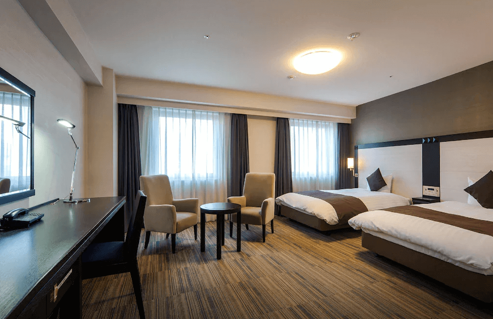 【大分住宿】大分大和ROYNET飯店 (Daiwa Roynet Hotel Oita) 的標準雙床客房,空間配置寬敞,除了舒適的床鋪外,靠窗處特別設置了兩張扶手沙發與圓桌,搭配長形辦公桌,無論是商務辦公或休閒放鬆都相當合適。