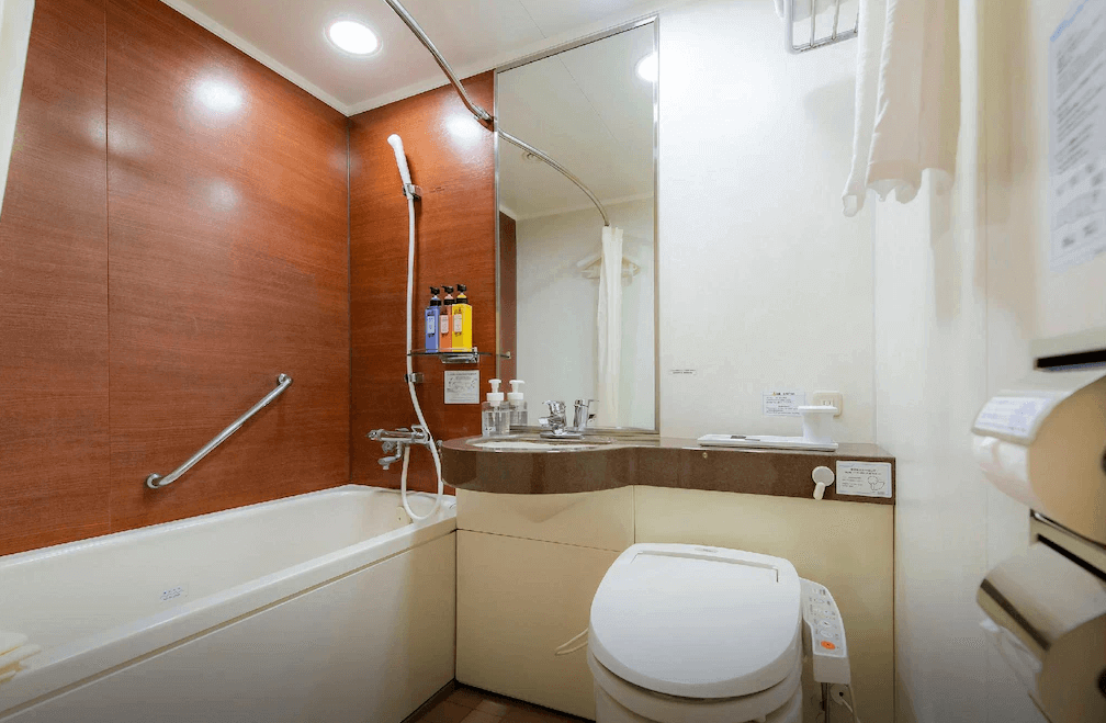 【大分住宿】大分大和ROYNET飯店 (Daiwa Roynet Hotel Oita) 的衛浴空間,採用深色木紋壁面增添質感,配備標準的浴缸與免治馬桶,整體環境乾淨明亮,提供旅客舒適的盥洗體驗。