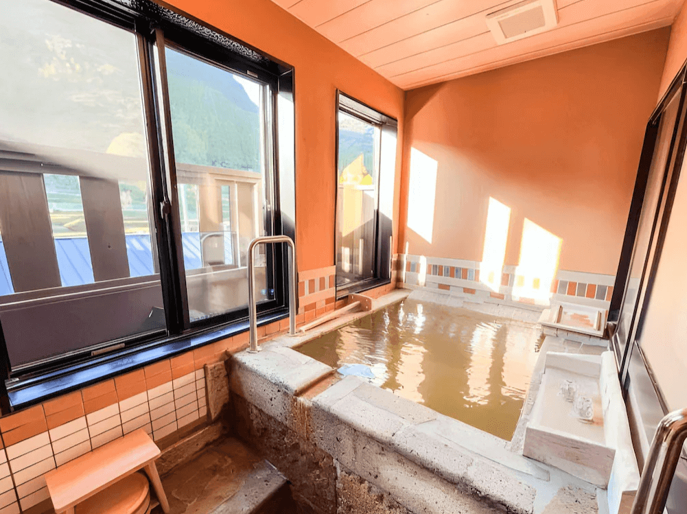 【霧島住宿】小鹿野溫泉美肌之湯飯店的私人湯屋，石砌浴池內注滿了獨特的琥珀色溫泉水，窗外可眺望寧靜的田園風光。