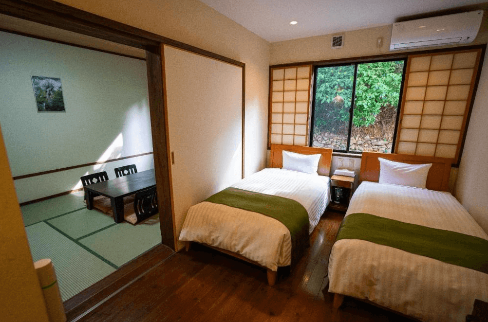 【屋久島住宿】「屋久島Manten旅館（Yakushima Manten Ryokan）和洋混合客房，設有雙床與相連的日式塌塌米間，窗外可見綠意景觀，房間溫馨舒適。」