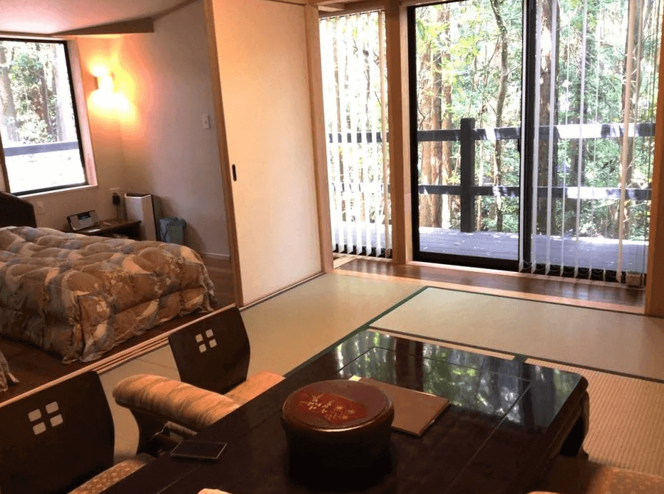 【屋久島住宿】「屋久島Manten旅館（Yakushima Manten Ryokan）森林景觀客房，房內配置和室座桌與床鋪，大片落地窗可欣賞屋久島林間景色，氛圍安靜放鬆。」