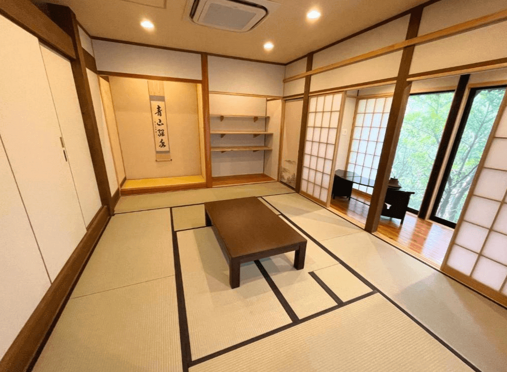 【屋久島住宿】「屋久島Manten旅館（Yakushima Manten Ryokan）寬敞和室，設有塌塌米地板、拉門與傳統壁龕，窗邊可見森林景觀，展現典雅日式風格。」