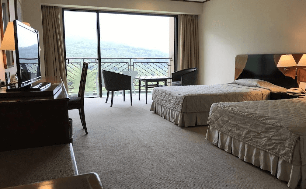 【屋久島住宿】「屋久島岩崎飯店（Yakushima Iwasaki Hotel）山景雙床房，寬敞明亮的房間設有陽台，可眺望綠意盎然的山景，房內配置兩張單人床與書桌。」